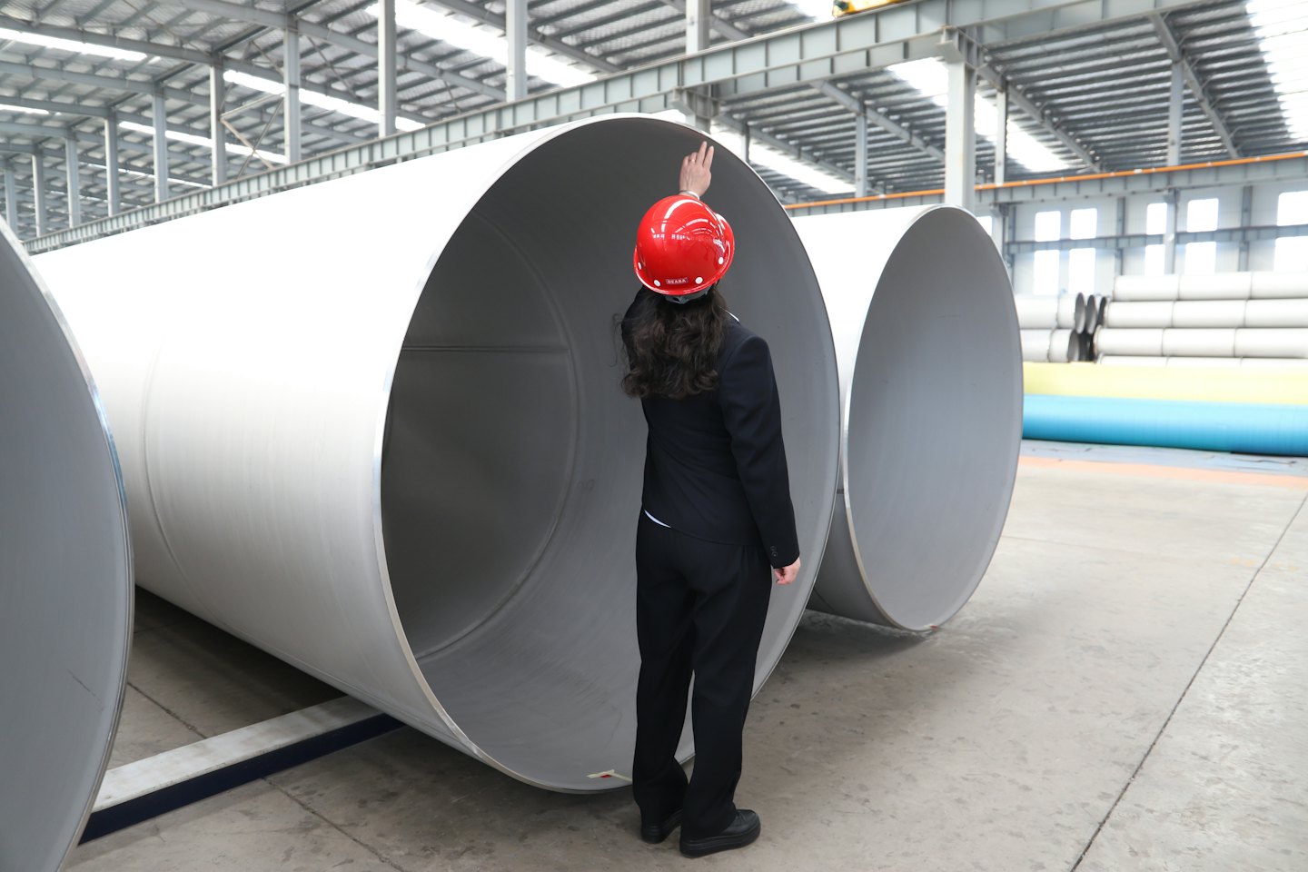 Ingenieur met rode helm wijst naar fabriekspijpen.