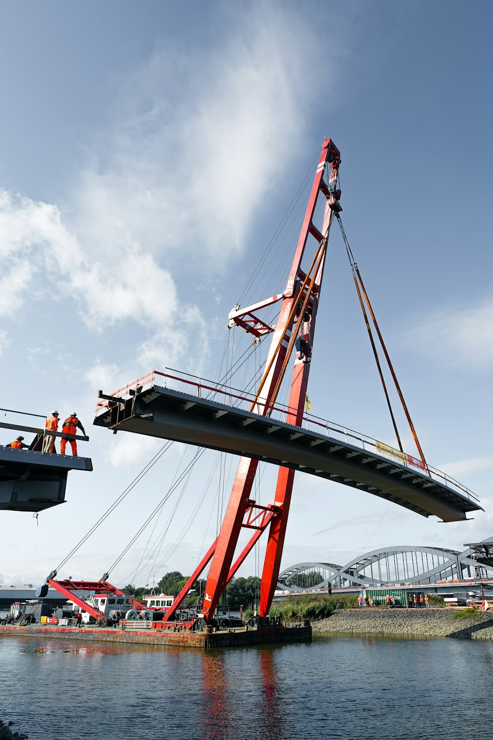 Een bouwkraan tilt een brugdeel boven het water.